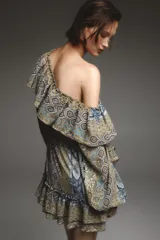 Vestido corto con estampado paisley en tonos ocre, azul y marrón. Tiene escote recto con volantes, mangas largas abullonadas con puños elásticos y cintura elástica.