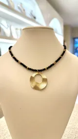 Collar corto de cuentas facetadas negras y doradas, con dije circular dorado.