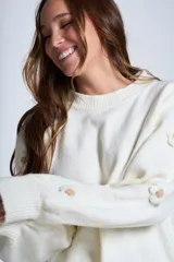 Sweater color crema de hilado frizado con cuello redondo y mangas largas. Presenta apliques de flores en los hombros y mangas.