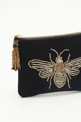 Bolso de mano tipo sobre rectangular de terciopelo negro con cierre dorado y flecos de mostacillas doradas. Presenta un bordado de abeja con canutillos dorados en el frente.