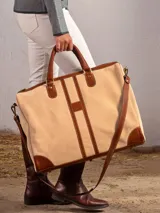 Bolso de mano confeccionado en cuero de color verde con detalles en marrón. Cuenta con dos asas superiores, una correa larga ajustable y removible, y cierre de cremallera. El diseño incluye franjas verticales decorativas en el centro y refuerzos en las esquinas inferiores.