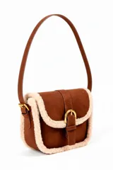 Cartera tipo bandolera color marrón con detalles de piel sintética color crema en los bordes. Tiene una solapa frontal con cierre de hebilla dorada y correa fina ajustable.