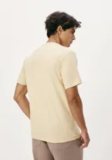 Camiseta blanca de algodón con cuello redondo y mangas cortas. Estampa rectangular con borde negro que contiene la frase "NATURAL ATMOSPHERE" en letras mayúsculas y una imagen de montañas y mar.