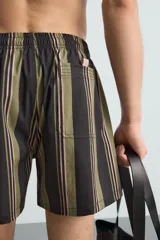 Bañador corto de tejido técnico con rayas verticales en tonos negro, verde oliva y rosa. Cuenta con cintura elástica ajustable con cordón, bolsillos laterales y trasero.