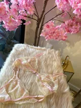 Conjunto de lencería de encaje floral en tonos rosa y crema, compuesto por un corpiño triangular sin aro con breteles finos regulables y una tanga regulable.