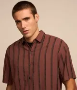 Camisa masculina de corte relajado, confeccionada en cáñamo, algodón y poliéster. Presenta cuello inglés, mangas cortas y rayas verticales texturizadas.