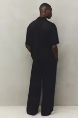 Pantalón cargo negro de corte holgado, con cintura elástica ajustable con cordón, bolsillos laterales al bies, bolsillos tipo cargo con solapa y botón a presión en las piernas y bolsillos traseros con solapa y botón a presión. Cuenta con pliegues cosidos en las rodillas y cordón ajustable oculto en el bajo.