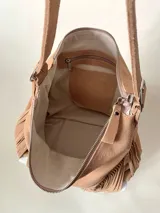 Bolso tipo hobo color tostado, hecho de cuero con flecos largos en el frente y dos bolsillos con cierre. Tiene una manija regulable con hebillas metálicas.