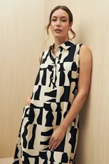 Vestido camisero largo con estampado geométrico en blanco y negro, de silueta amplia y caída fluida. Presenta cuello clásico, cartera central con botones y diseño sin mangas.