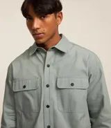 Camisa marrón de manga larga, confeccionada en sarga, con cuello inglés, abotonado delantero, bolsillos en el pecho con solapa y puños abotonados.