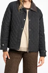 Campera capitoneada de color negro con diseño de rombos, cuello camisero en contraste de color marrón, cierre frontal con cremallera y solapa con botones a presión. Presenta mangas largas con puños ajustables y un calce entallado.