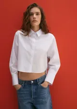 Camisa blanca crop de popelina de algodón, corte regular, manga larga con puños abotonados, cuello camisero y cierre frontal con botones.