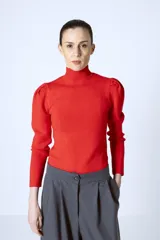 Polera roja de tejido de punto con cuello alto y mangas largas abullonadas en los hombros.