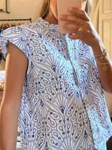 Camisa blanca con estampado de cachemir azul, cuello alto y mangas cortas con volantes.