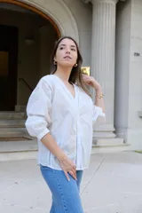 Blusa blanca de manga larga con elástico en puños, escote en pico y cierre frontal con botones. Detalles de bordados con hilado en tonalidad camel y acabado con entredoses a tono.