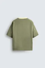 Camiseta color verde claro, de corte holgado, confeccionada en tejido de algodón con interior reversible de popelín. Tiene cuello redondo, manga corta y acabados con vivo combinado a contraste.