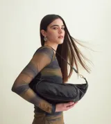 Bolso negro en forma de medialuna, confeccionado en piel brillante, con cierre de cremallera superior y correa extraíble con herrajes dorados.