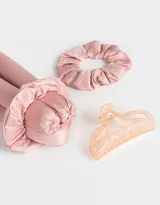 Set de accesorios para el cabello que incluye un rizador sin calor de tela satinada color rosa, dos scrunchies de tela satinada color rosa y un broche de plástico color durazno.