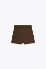 Shorts color marrón confeccionados en hilatura con algodón. Tiro alto y cintura doble con trabillas, bolsillos laterales y falso bolsillo con solapa en delantero. Detalle de costuras a contraste y cierre frontal con cremallera y ganchos metálicos.