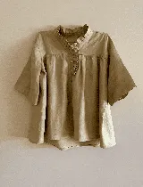Blusa color beige de lino con cuello mao con volados, manga corta abuchonada, calce holgado y acceso frontal a través de cartera de botones de nácar.