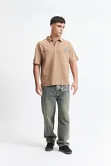 Remera polo color beige con textura acanalada, corte oversize, cuello clásico con botones y logo estampado en el pecho.