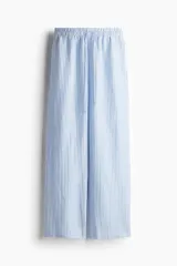 Pantalón de corte holgado en tejido liviano de mezcla de lino a rayas verticales celestes y blancas. Modelo de tiro alto con cintura elástica y cordón para ajustar fino, bolsillos laterales discretos y piernas rectas.