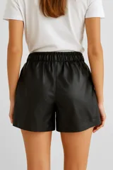 Short negro de cuero sintético, tiro alto, con cintura elastizada y cordón ajustable.
