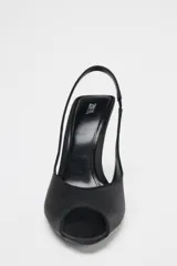 Zapato de tacón destalonado color negro con efecto satinado, punta fina, abertura delantera y tira trasera elástica. Tacón alto fino.