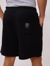Bermuda deportiva gris confeccionada en 60% algodón y 40% poliéster, con cintura elástica ajustable con cordón.