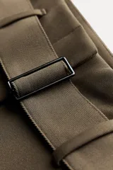 Pantalón de tiro medio color verde oliva, con cintura con trabillas, bolsillos laterales ocultos, cinturón ajustable con hebilla metálica, pinzas delanteras y cierre frontal con cremallera, botón y gancho metálico.