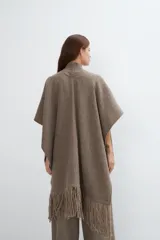 Ruana color crema de lana fina con flecos en el ruedo y bolsillos delanteros.
