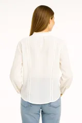 Blusa blanca de manga larga con cuello mao con lazo y cierre frontal con botones.