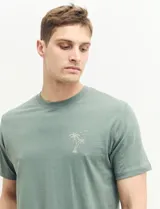 Remera verde con estampado en la espalda de una playa con palmeras y la frase "Ride the waves".