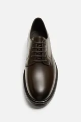 Zapato de vestir tipo derby color marrón oscuro, con parte superior lisa, horma redonda y suela a contraste.