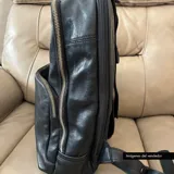 Mochila negra de cuero vacuno con forro de gabardina de algodón, compartimento acolchado para laptop de hasta 14 pulgadas, bolsillo frontal con cierre y cierres metálicos plateados.