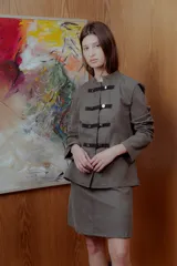 Conjunto de chaqueta y falda color gris verdoso. La chaqueta es de corte recto, con cuello mao y cierre frontal con pasamanería y botones metálicos. La falda es recta, a la rodilla.