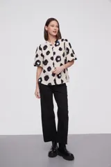 Blusa de manga corta con estampado de manchas negras y azules sobre fondo crema, cuello mao y cierre frontal con botones.