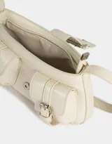 Cartera baguette color crudo de cuerina con correa regulable y hebillas frontales decorativas.