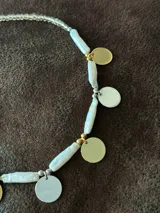 Collar corto con perlas de río naturales, cuentas metálicas de acero quirúrgico, medallitas bañadas en plata y oro y mostacillas. Se cierra con cadena de acero quirúrgico y ganchito para regular el largo.