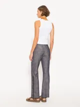 Pantalón de lino con apariencia denim, tiro bajo y corte recto. Presenta detalles de galón con flecos y cadenas en los laterales inferiores.