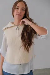 Chaleco corto de punto color crudo, con cuello alto, medio cierre frontal y botones laterales.