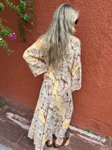 Vestido largo de seda con escote en V y mangas amplias, presentando un estampado paisley en tonos beige, rosa pálido y toques de amarillo.