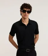 Camisa polo negra de manga corta, confeccionada en poliamida y elastano, con cuello inglés abotonado y tecnología Performance que proporciona mayor comodidad térmica, elasticidad y secado rápido.