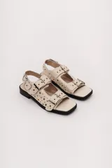 Sandalias bajas color crema con apliques de tachas metálicas y hebillas plateadas.