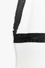 Vestido midi blanco de tejido elástico, con cuello halter, escote pico, falsos bolsillos de vivo con botón y acabados a contraste en negro.