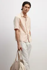 Camisa de manga corta color rosa claro, con cuello inglés, tapeta lisa, bolsillo superior abierto, canesú en la espalda y bajo recto.