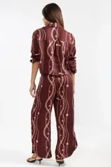 Camisa corta de lino color borgoña con estampado de cadenas y flores rosadas. Tiene cuello clásico, mangas largas y cierre frontal con botones.