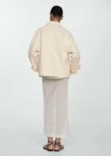 Chaqueta color crema estilo tejana vaquera, de corte oversize, con cuello camisero, cierre frontal de botones, mangas largas con puños abotonados, dos bolsillos de parche con solapa en el pecho y bolsillos laterales.