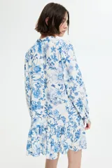 Vestido corto de viscosa con estampado floral en tonos azules. Tiene cuello mao, botones frontales, mangas largas abullonadas con puños abotonados y falda con volantes.