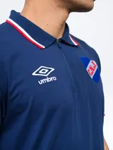 Remera polo azul con cierre, puños y cuello con detalle tricolor. Incluye logo de Umbro y escudo del Club Nacional de Football.